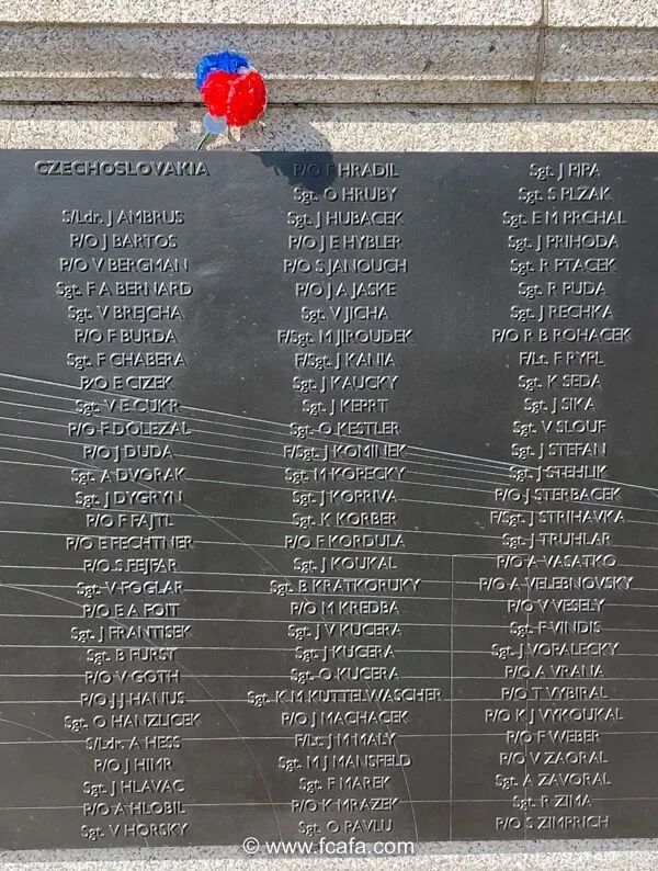 Pamětní deska s jmény pilotů Československého letectva na památníku v Anglii, s červenou a modrou kyticí připnutou na vrcholu.
