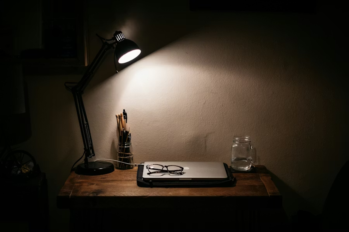 Desk lamp illuminating a table with a laptop and notes, representing late-night online activities.