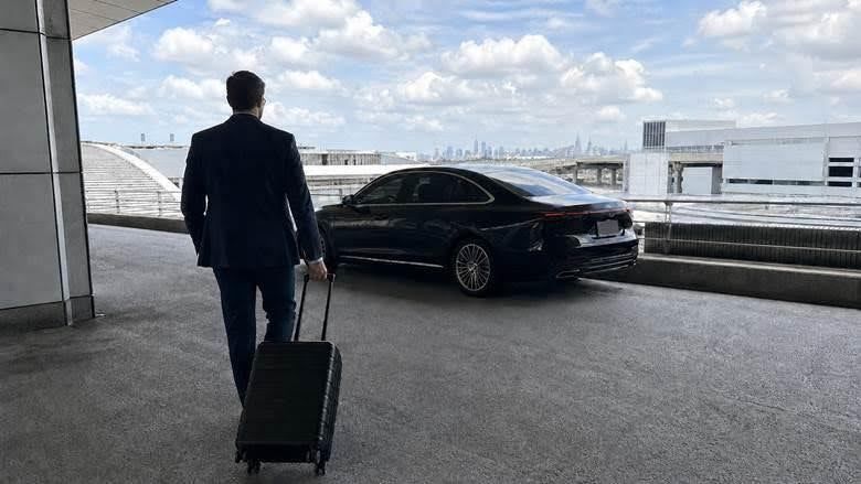 A traveler and a waiting black car, the New York skyline in the distance