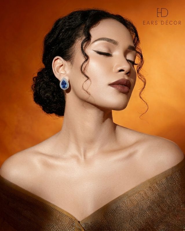 Woman wearing blue sapphire and diamond halo teardrop earrings in an Ears Décor jewelry advertisement