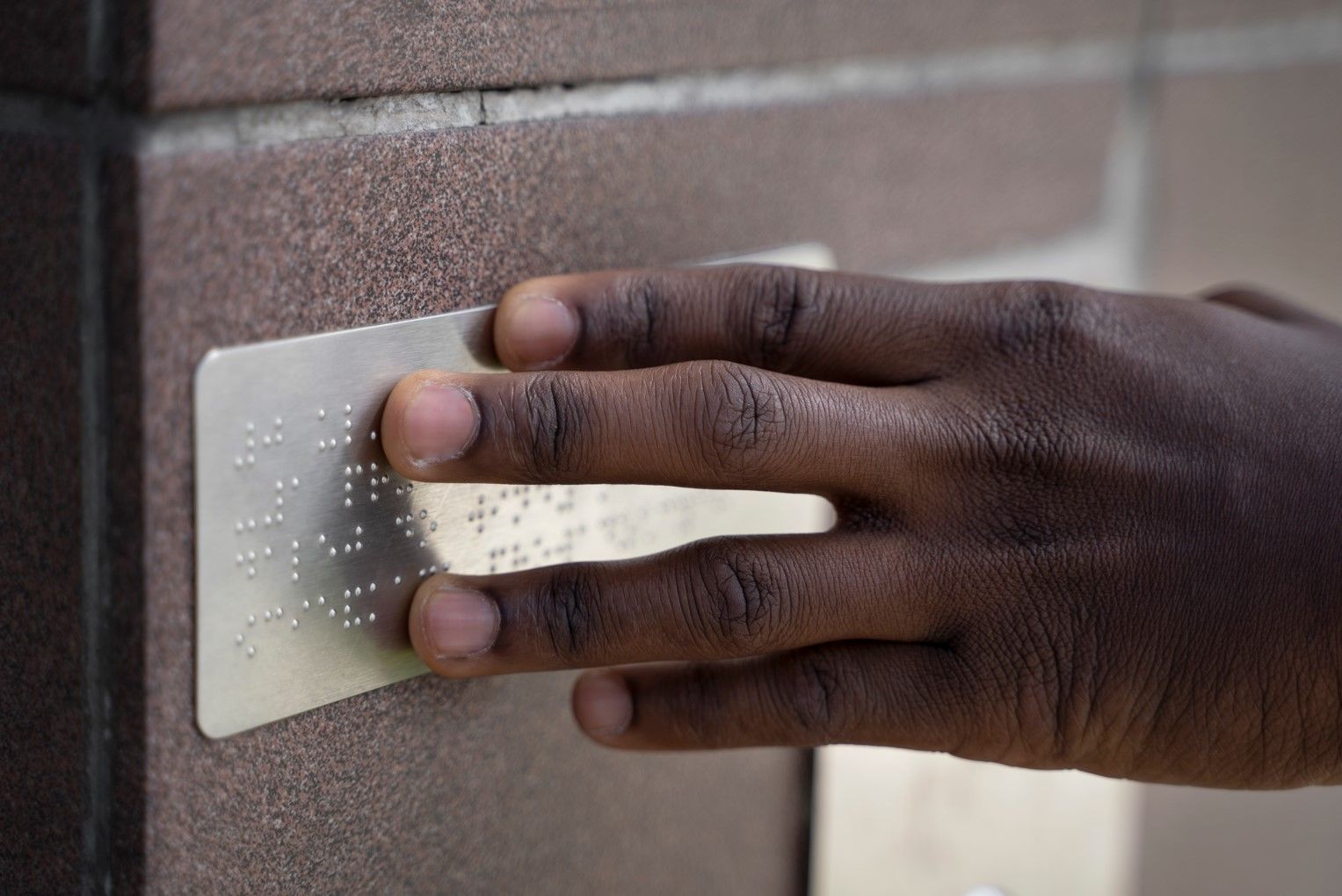 Hand voelt aan brailleplaatje op een muur