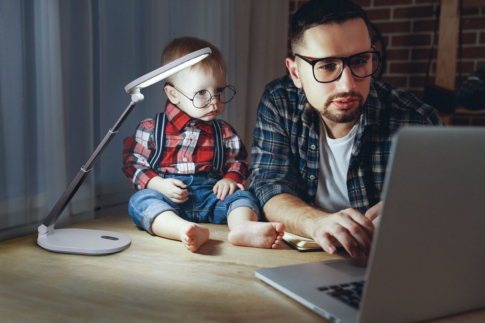 Man kijkt naar de computer met zijn 18 maanden oude kind dankzij een Daylight-lamp