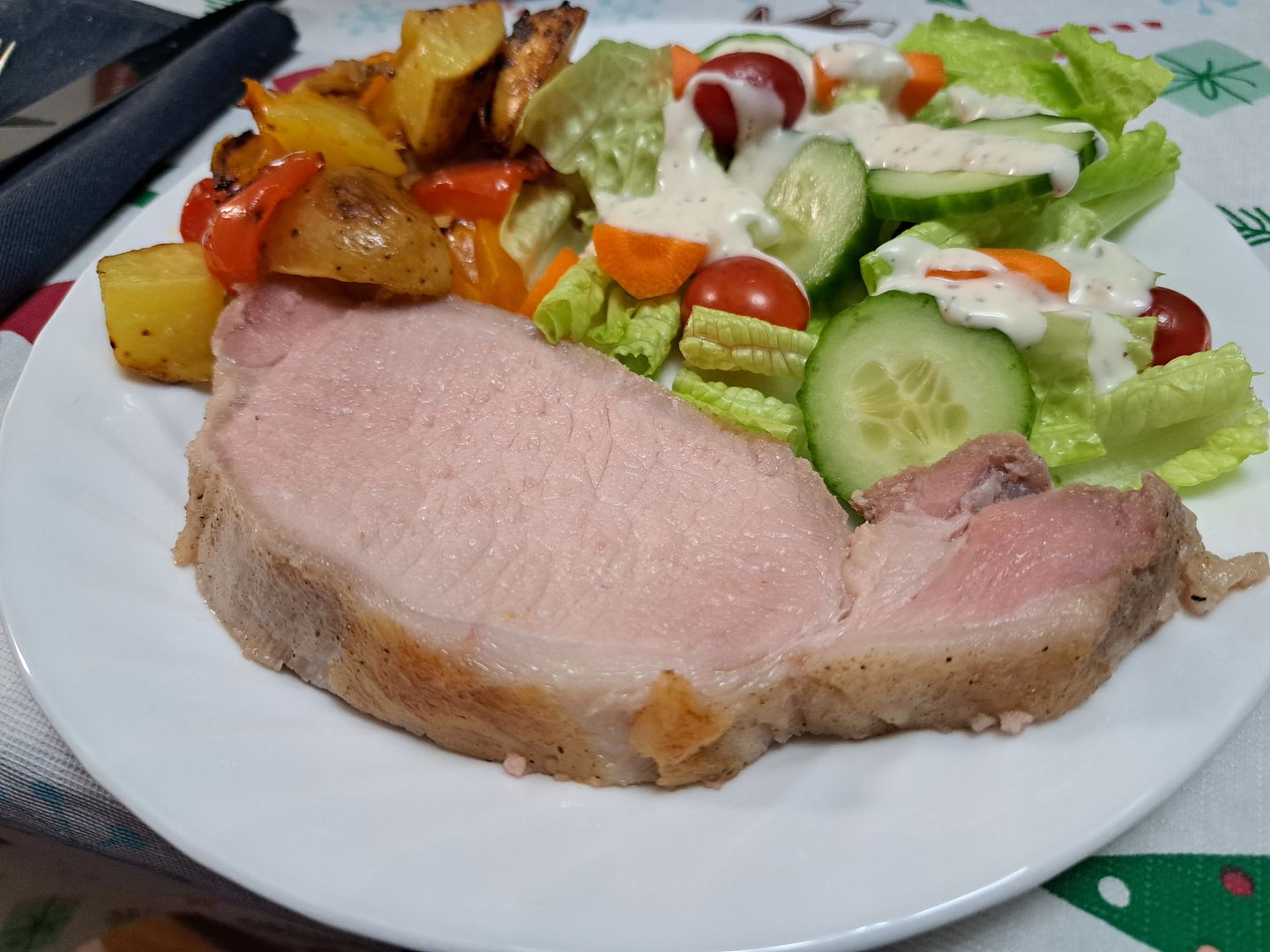 A slice of pork loin on a dinner plate, served with roasted potatoes and sweet peppers and a tossed green salad.
