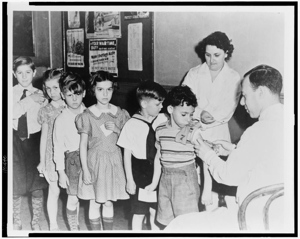 Photograph shows school children waiting in line for immunization shots at a child health station in New York City, N.Y.