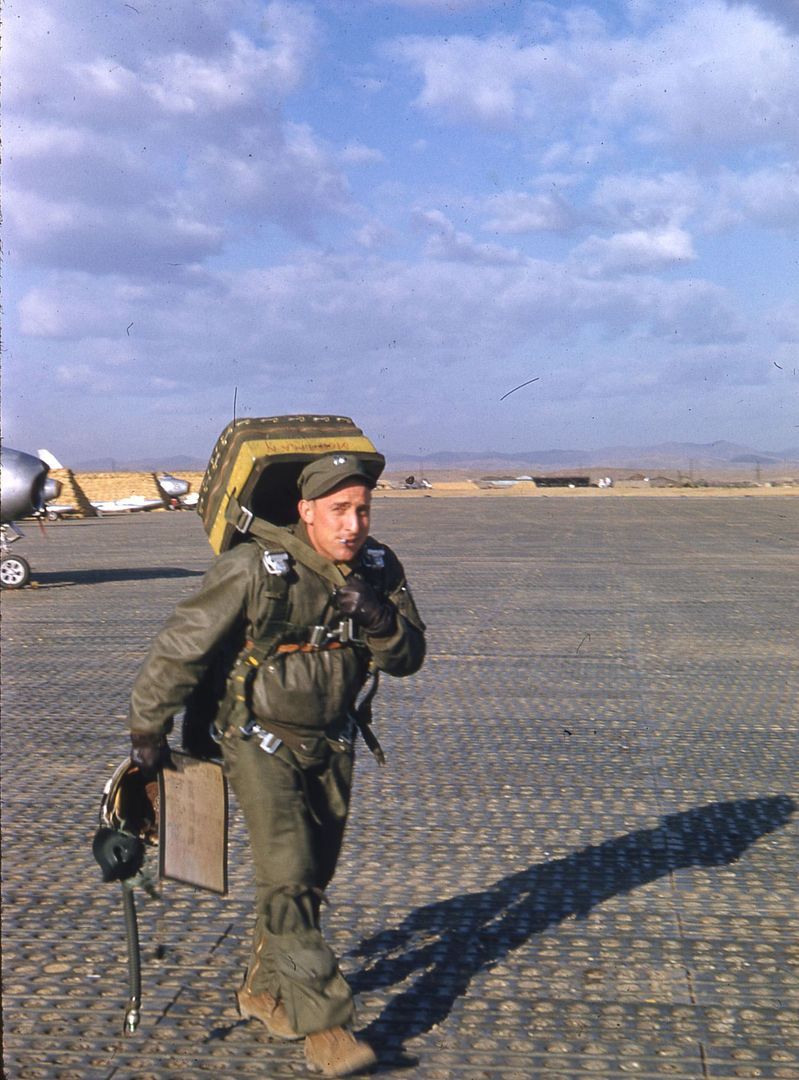 A_pilot_carrying_his_flight_gear_and_smoking_a_cigarette_walks_by_cameraman._Several_North_American_F_86_Sabre_jets_are_in_the_background..jpg