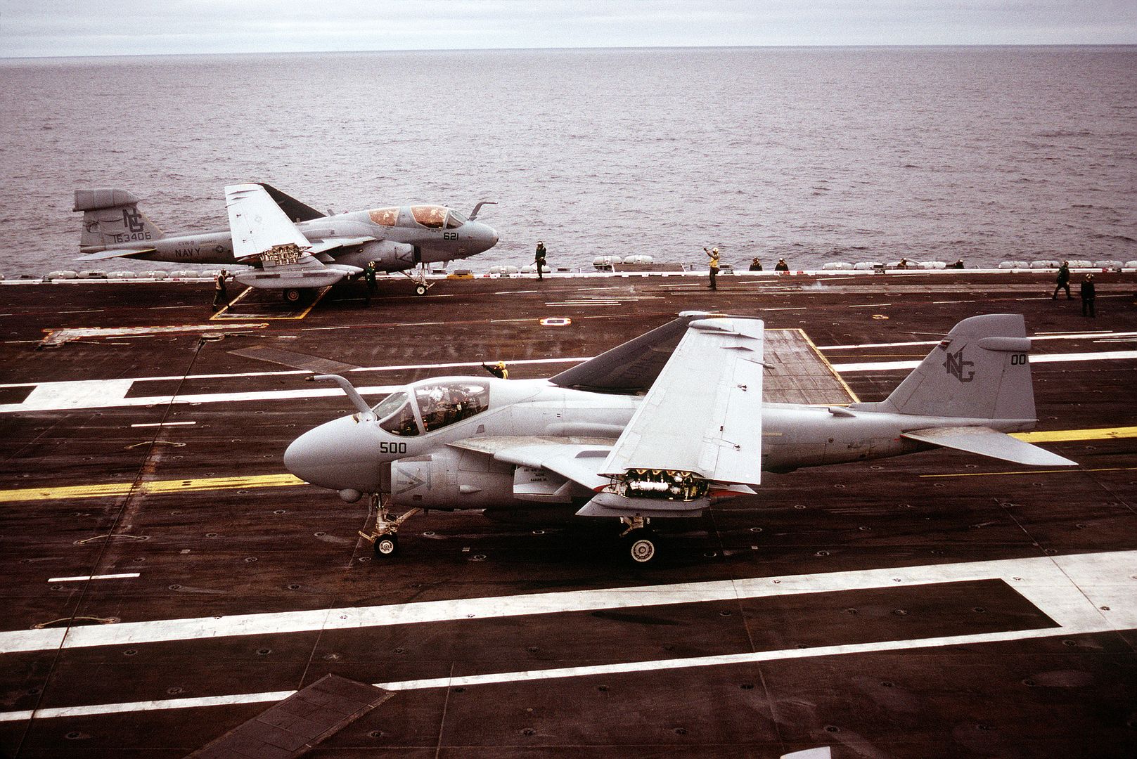 An A 6E Intruder Aircraft Of Attack Squadron 165 Taxis On The Flight Deck Foreground As An EA 6B Prowler Aircraft Background Of Tactical Electronic Warfare Squadron 138
