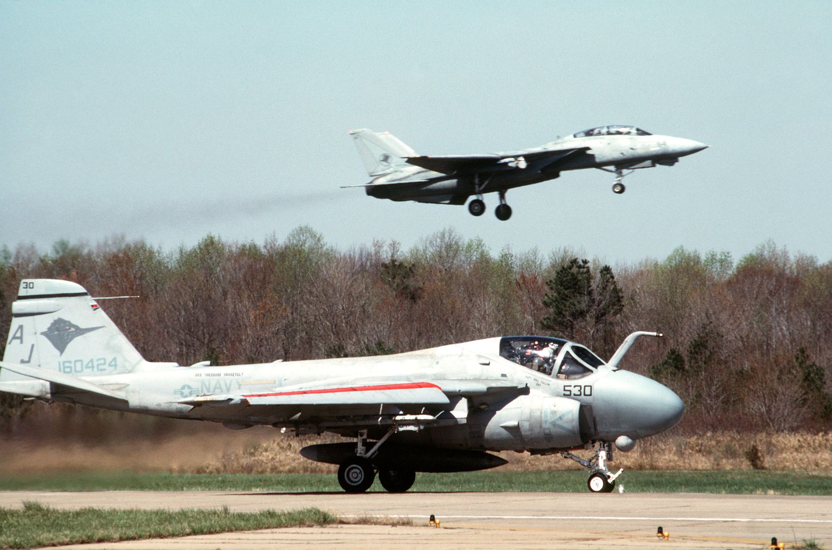 An Attack Squadron 36 A 6E Intruder Aircraft Rolls Along A Runway As A Fighter Squadron 14 F 14A Tomcat Aircraft Passes Overhead
