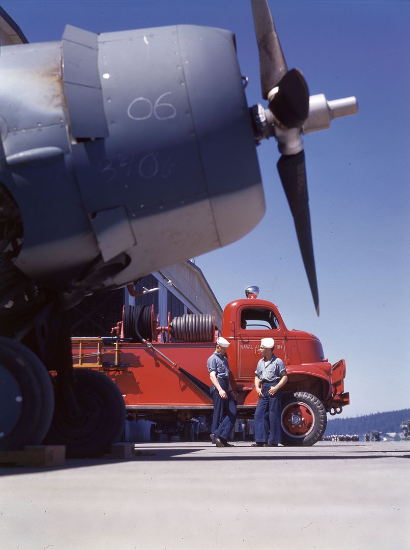 Two Members Of Alert Crew Stand By Fire Truck At Naval Air Station With F4F In Foreground