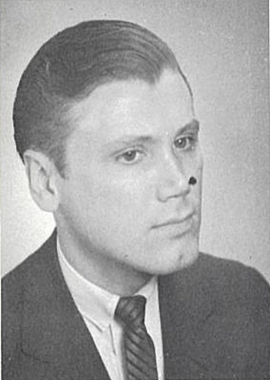 George Bergman Photo in SFSC 1962 Commencement Program. A black and white photo shows a white man with dark eyes, a cleft chin, and his short, dark hair combed back. He is looking to the side with a pleasant expression and is wearing a dark suit with a white collared shirt and tie with diagonal stripes. A dark spot is on the photo near his nose.